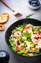 Strawberry, shrimp and herbs salad with arugula, lettuce, avocado and almond slices, gray table. Fresh useful dish for healthy eating. Top view