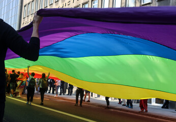 Photo of LGBT flag. People hold the rainbow flag on the background of a large flag in Krakow, Poland
