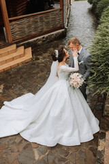 Fototapeta premium Wedding photo. The bride in a voluminous white dress and a long veil stands with the groom in the park on a stone path. View from above. Portrait of the bride. Beautiful curls. Beautiful makeup.
