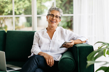 Enjoying retirement with mobile technology, senior woman sitting on a couch with a smartphone