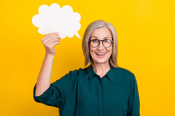 Photo of cheerful aged lady arm hold empty space cloud figure dialogue card isolated on yellow...