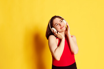 Portrait of beautiful, attractive young brunette girl listening to music in headphones against yellow studio background. Concept of youth, human emotions, lifestyle, beauty, ad