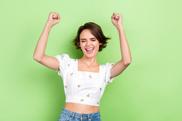 Photo of charming crazy lady celebrate victory raise fists glad expression wear white crop shirt isolated green color background