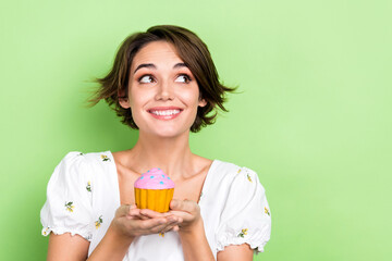 Photo of cute adorable lady wear white crop top holding cupcake looking empty space isolated green color background