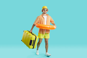 Joyful young man with suitcase and inflatable circle goes on summer vacation to seaside resort....