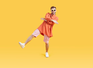 Full body photo of cool funny young guy with unshaven beard dancing wearing bright summer casual clothes and white sneakers isolated on a yellow background. Man having fun in studio.