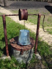 Rural well with clean water. A zinc bucket tied to a well of water. - 613157563