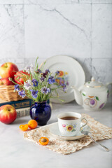 Summer still life: tea in a vintage cup, apricots, apples, books and cornflowers - 613157999
