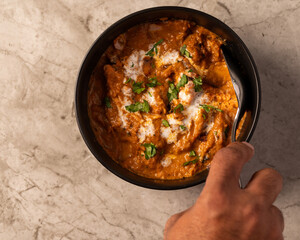 Hands Preparing a Bowl of Buter Chicken and Rice on a Marble Counter