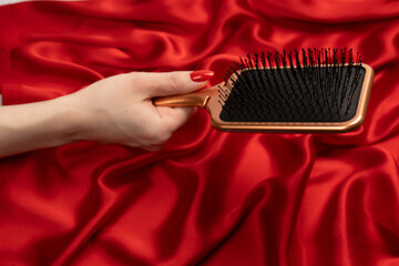 A red hairbrush in woman hand with red nails ion a red background.