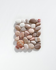 Top view close up colored pebbles sea stones with dark shadows on white background. Creative  Square pattern from stone natural shade. Minimal summer flat lay, spa and relaxation concept.