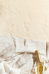 Summer minimal flat lay with wine glasses, bottle sparkling wine in mesh bag on beige beach towel on sand, sun shadows. Summer lifestyle pastel colored aesthetic photo. Top view background