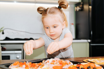 Cute child cooking food in kitchen, little girl using pizza cheese. Children's culinary hobby