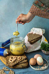Woman takes the pickled herring out of glass jar to make sandwiches with eggs, arugula and cod roe paste on crisp breads.