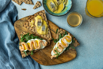 Swedish meal. Crisp breads with different toppings : pickled herring in mustard sauce, egg, arugula and cod roe paste, juice and coffee on blue background.