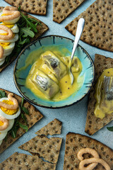 Bowl with pickled herring in mustard sauce surrounded with crisp breads with different toppings.