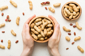 Woman hands holding a wooden bowl with close peanuts. Healthy food and snack. Vegetarian snacks of...