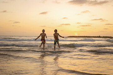 Fototapeta na wymiar Happy teenager boys, running and playing on the beach on sunset, splashing water and jumping on the sand
