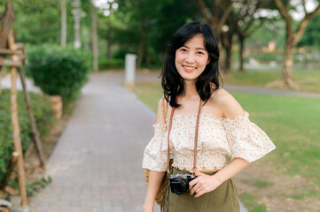 Portrait of asian young woman traveler with weaving hat and basket and a camera on green public park nature background. Journey trip lifestyle, world travel explorer or Asia summer tourism concept.