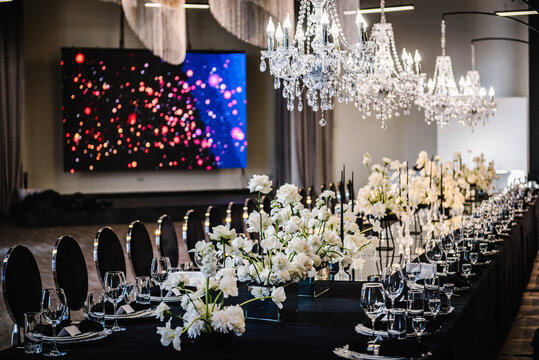 Luxury wedding reception. Trendy decor large chandelier for a birthday party. Table setting, setup. Banquet decoration composition flowers, candles in hall restaurant. Table covered black tablecloth.