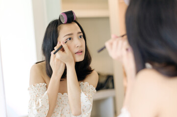 Fototapeta premium Beautiful young Asian woman applying makeup in front of the mirror. Lifestyle people concept. Advertisement for skin cream, anti-wrinkle cream, baby face