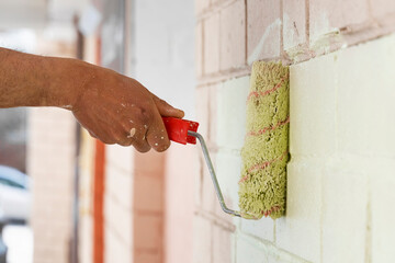 Worker painting a brick wall with a paint roller