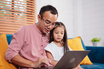 Obraz premium Cute little asian daughter with father working on laptop at home. single loving dad man shopping insurance to daughter by online technology.