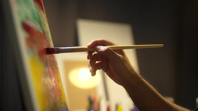 Close-up Moving Paint brush holding on hand of artist and painting on canvas work art with color oil painting at dark room workshop. Artist works and Creative on Abstract Oil Painting at night.