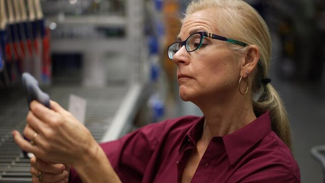Attractive mature woman looks closely at paint brush for home remodeling project.