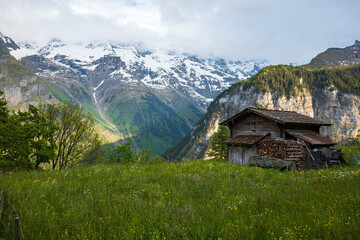 Fototapeta na wymiar Wooden shed or log cabin in the Swiss Alps. Sunny summer day, no people, snowy mountain range in the background