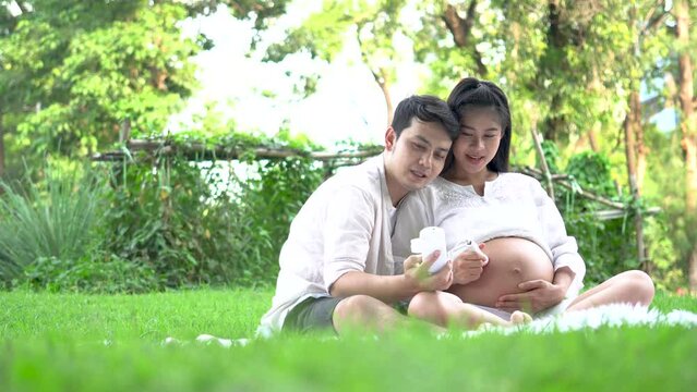 Happy Asian couple pregnant woman and husband using fetal doppler device for listening hear baby heartbeat device.

