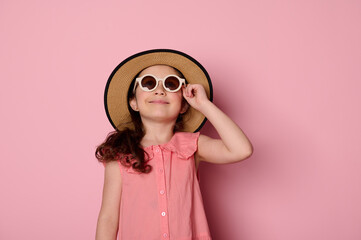 Mischievous Caucasian baby girl 6 years old, wearing sunglasses, straw hat and summer sundress,...