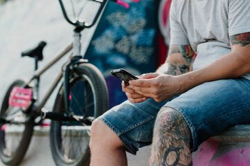 Cropped picture of an urban middle-aged tattooed man sitting in a skate park next to his bmx bike...