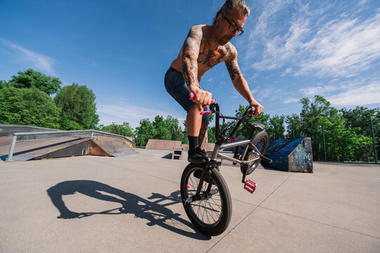 Wide angle view of an urban tattooed man doing tricks and stunts with his bmx in a skate park.