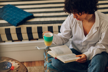 Portrait of a beautiful woman reading a book and drinking coffee at home