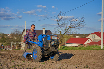 a man plows with a walk behind tractor at sunset,a farmer works in the village in the field cultivates soil for planting