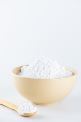 Tapioca starch in a bowl and wooden spoon on a light background.