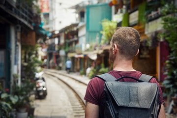 Man with a backpack walking through narrow Train Street. Railroad track between residential buildings in Hanoi Vietnam. .