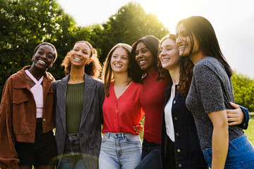 Young multiracial women having fun outdoor - Diverse female friends hugging each other during summer vacations at city park - Focus on center faces