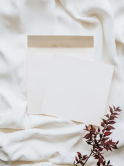 White blank paper sheet card mockup, envelope and dry floral branch on neutral white textile background.