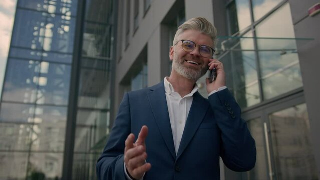 Adult middle-aged businessman walk in city having cell call negotiate senior mature man business investor employer talking mobile phone entrepreneur talk cellphone walking near office company building