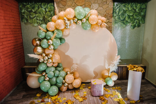 Reception at birthday party. Arch decorated green, brown, golden balloons, dry autumn leaves for wedding ceremony. Celebration baptism. Trendy autumn decor. Photo wall decoration space, place for text