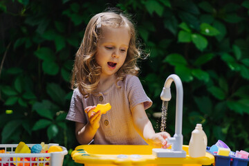 A little girl playing with toy kitchen in garden. Child play outdoors in summer. Play area...