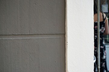 Grauweiße Hausfassade mit offener Eingangstür und Anschnitt von Kundin in schwarzem ärmellosen Hosenanzug mit Muster vor Kasse in Café in Stadt bei Sonne am Abend im Sommer