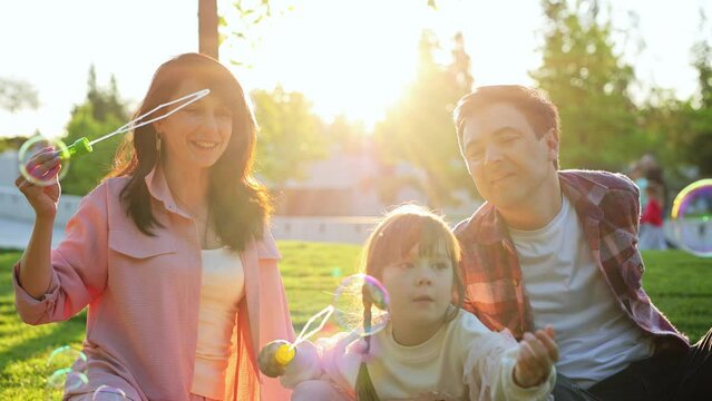 Cheerful, happy family having fun and blowing soap bubbles in the park at sunset.