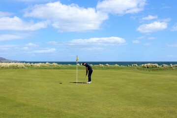 A man putting on a golf green on a links golf course with the ocean in the background on a beautiful sunny day in the highlands in Brora, Scotland