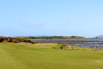 An incredible view of a golf hole in Scotland with the ocean in the background in Inverness, in the highlands of Scotland during spring with the gorse bush in full yellow bloom and beside the ocean