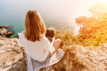 Freelance woman working on a laptop by the sea, typing away on the keyboard while enjoying the beautiful view, highlighting the idea of remote work.