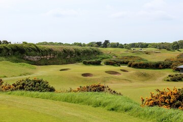 An incredible view of a classic links golf hole with pot bunkers in Scotland with the ocean in nearby outside of St. Andrews, Scotland