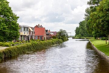 Obraz premium Houses along a canal in the countryside of Netherlands on a cloudy summer day